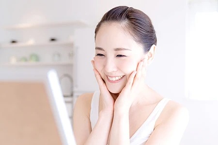 鏡を見て笑顔で頬に触れる女性患者
